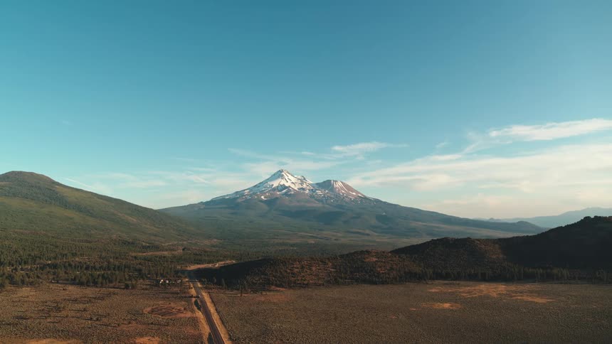 Dirt road passes through fields toward snow covered twin peaked mountain