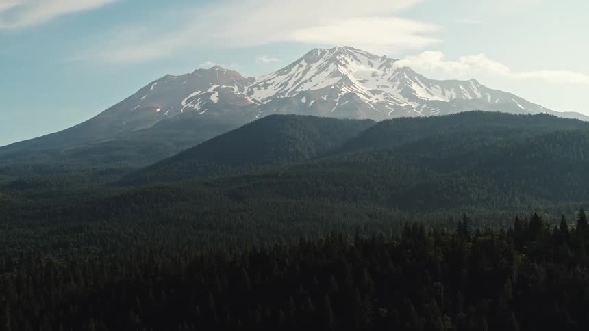 Forested mountains with snow covered mountains in the distance