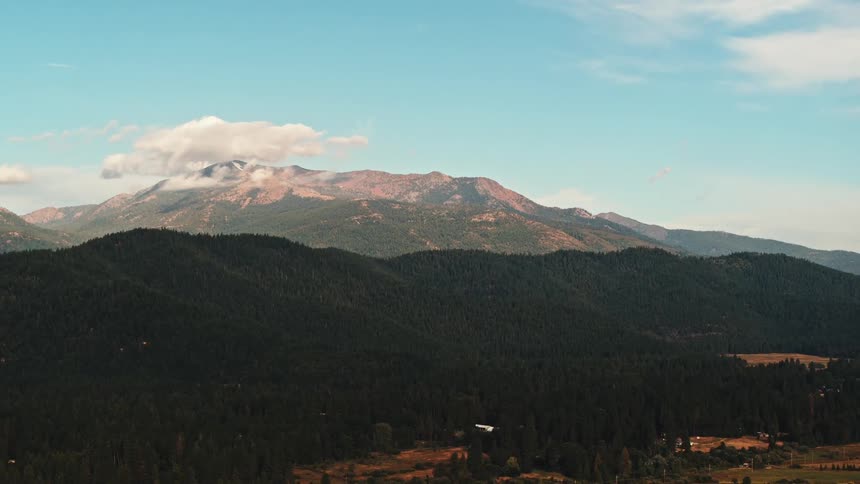 A landscape with hills trees a mountain range the sky and clouds in the background