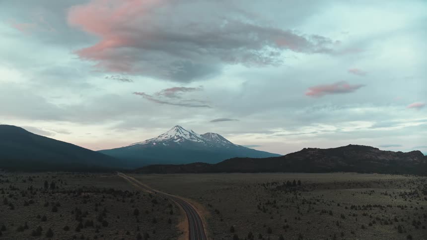 A snow capped mountain looms of a vast grassland on a cloudy day