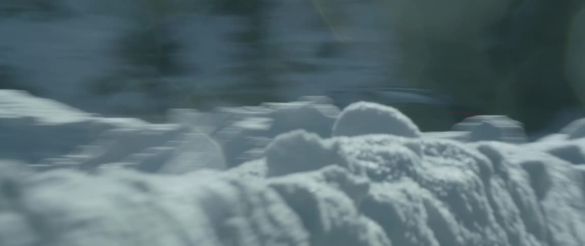 A black car speeds down a road surrounded by snow