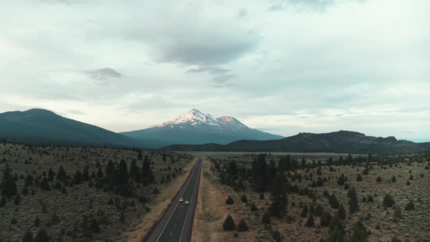 Vehicles pass each other driving along highway in opposite directions with snow covered mountain in background