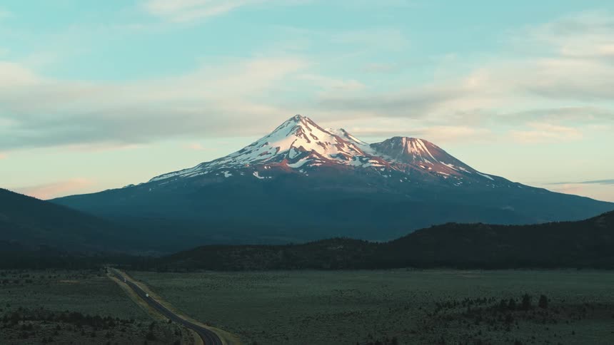A valley lays under the shadow of a snowy mountain peak