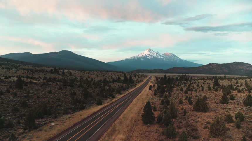 Road in the countryside near the snow covered peak of a mountain at sunset