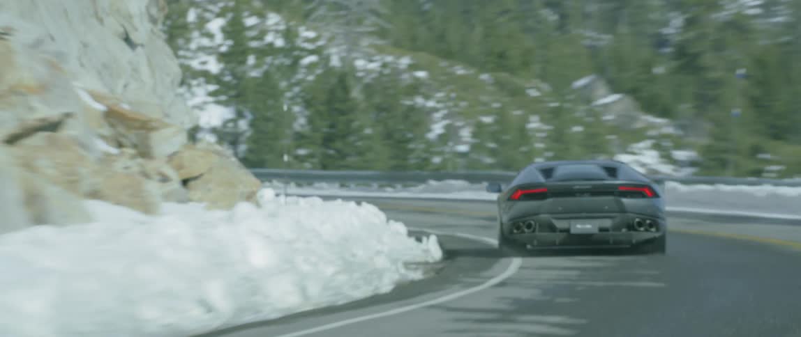 A black car speeds down a mountain road in the winter