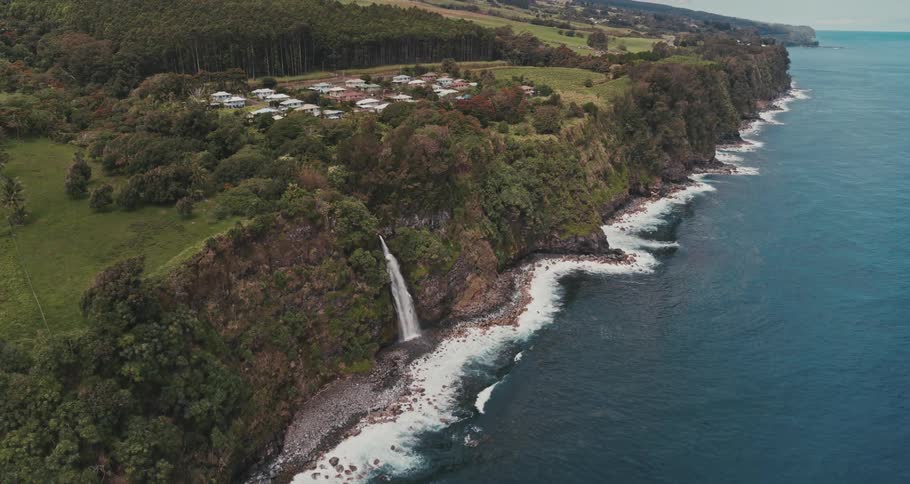 An aerial view of houses above the shore with a waterfall cascading down