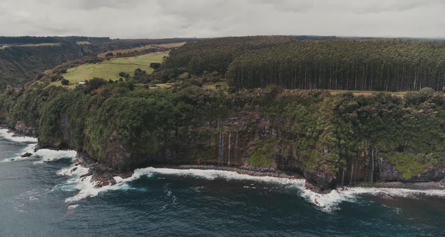 Ocean waves splash against a rocky shore below green cliffs