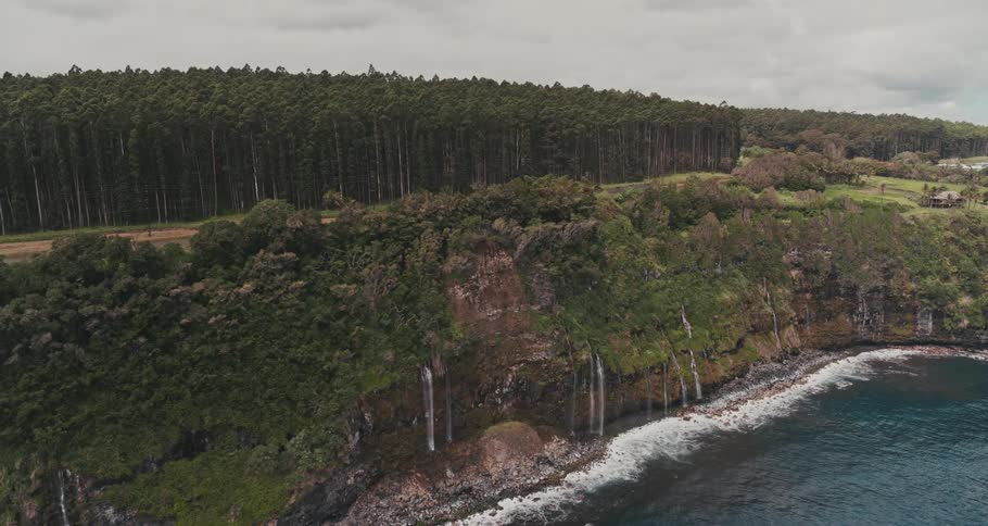 Waterfalls spill into the ocean from tall cliffs on the coast