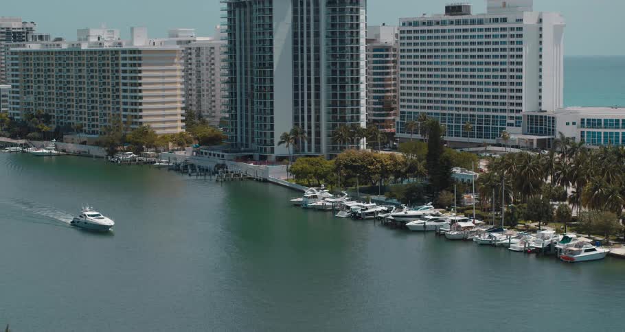 A marina with boats next to trees and buildings with the ocean sky and clouds in the background