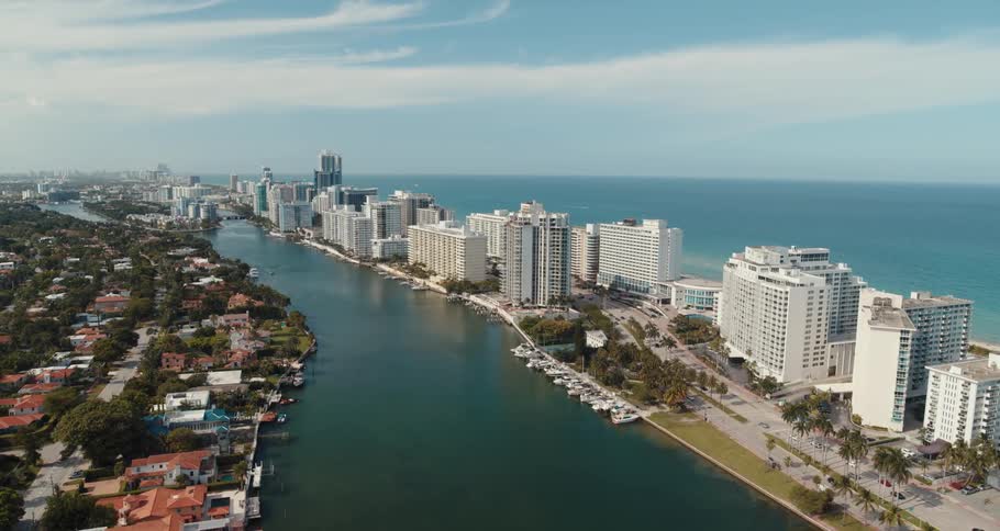 Traffic flows past buildings bordered on two sides by water across from homes