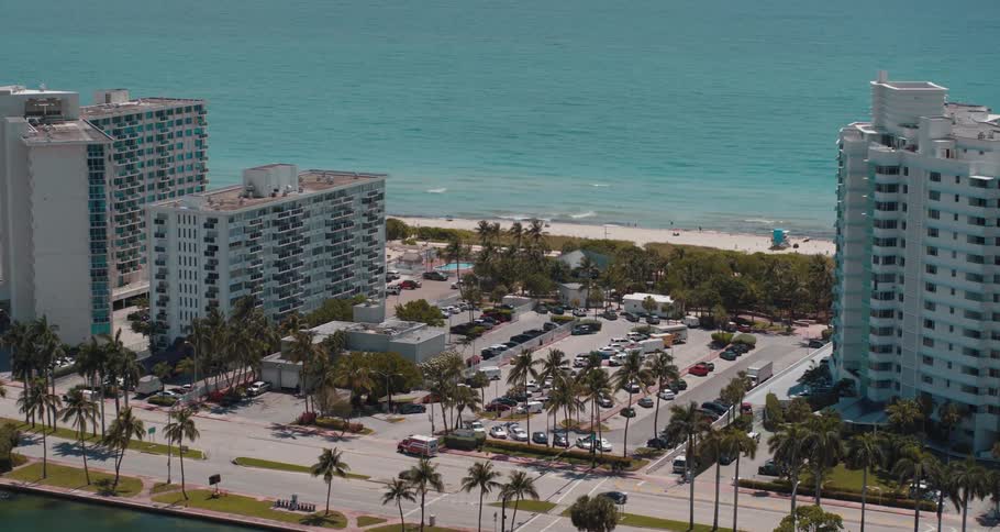 Buildings roads trees and vehicles next to the beach with the ocean sky and clouds in the background