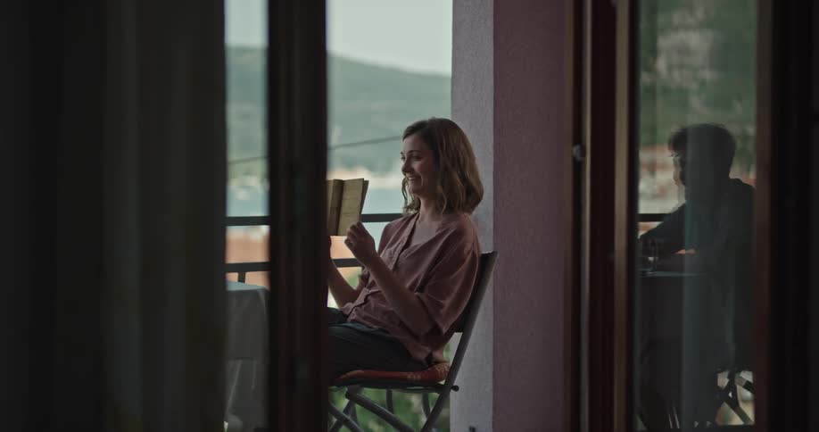 Woman sitting on a chair at a table in the apartment balcony near the beach