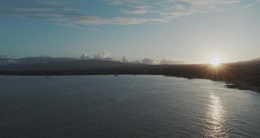 The sun peaks over the horizon to shine on a bay during the day