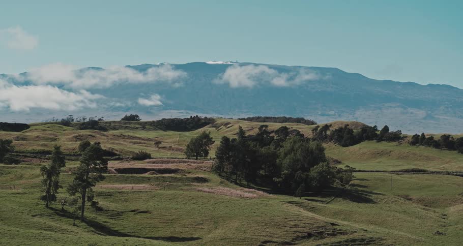 A landscape with trees a road and vehicles with a mountain range the sky and clouds in the background