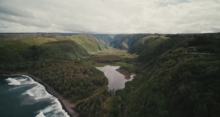 Waves hit the shores next to mountains that have a river winding through them