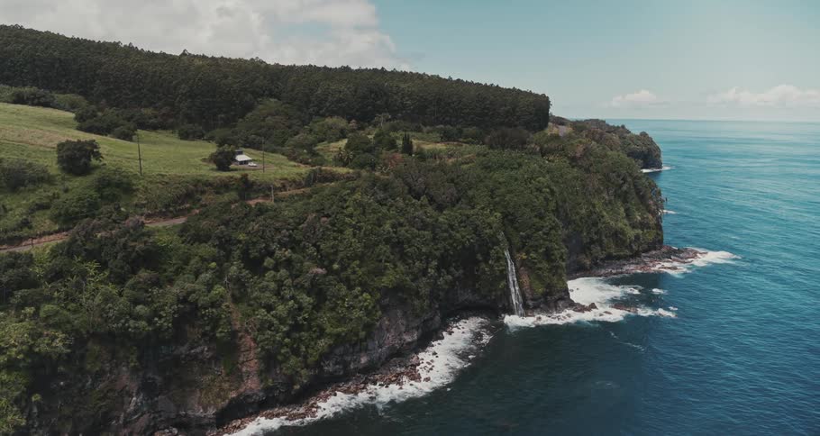 A waterfall surrounded by lush trees is flowing down a rock cliff into the ocean
