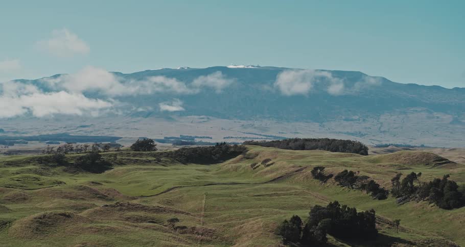 A pickup truck drives down a rural highway that runs through rolling hills near tall mountains