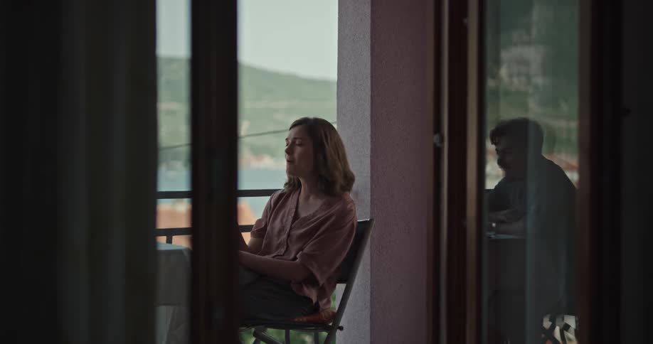 A woman eats slices of fruit at a table on a balcony with a man during the day