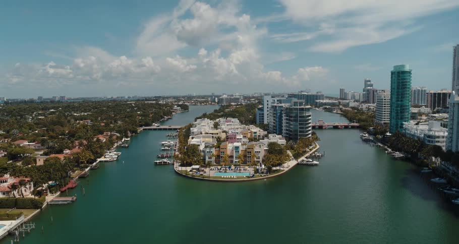 A canal with boats docked along the sides and a center island with buildings and swimming pools