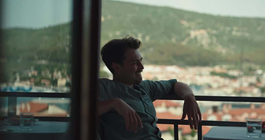 A man is sitting down talking and rests his arm on a rail