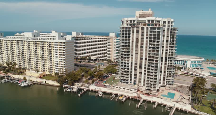 An aerial view of hotels on the shore with boats docked and cars driving on streets