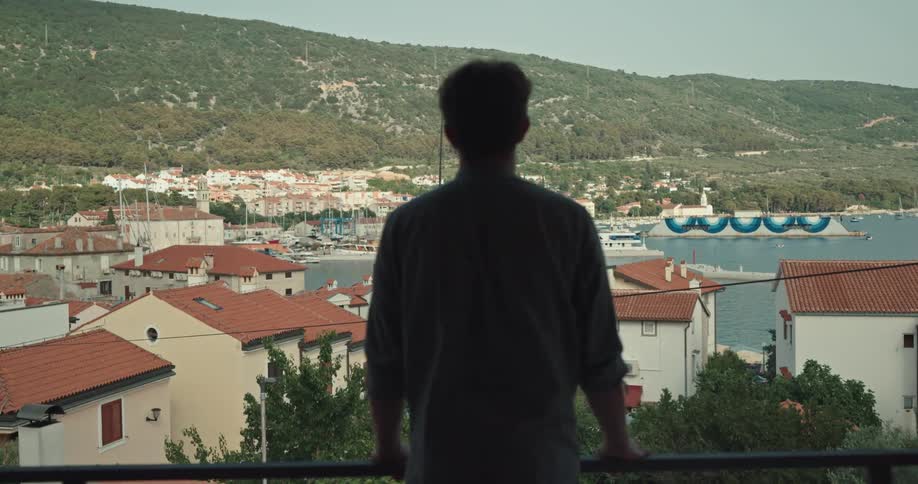 A man is standing on a balcony and looking at the horizon