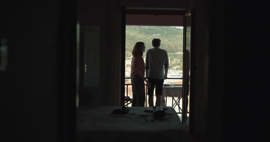 A woman bumps and yells at her husband aggressively on a hotel balcony before walking back into the room