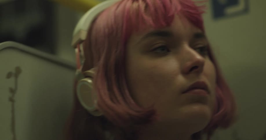 A young woman is wearing headphones while riding on the subway