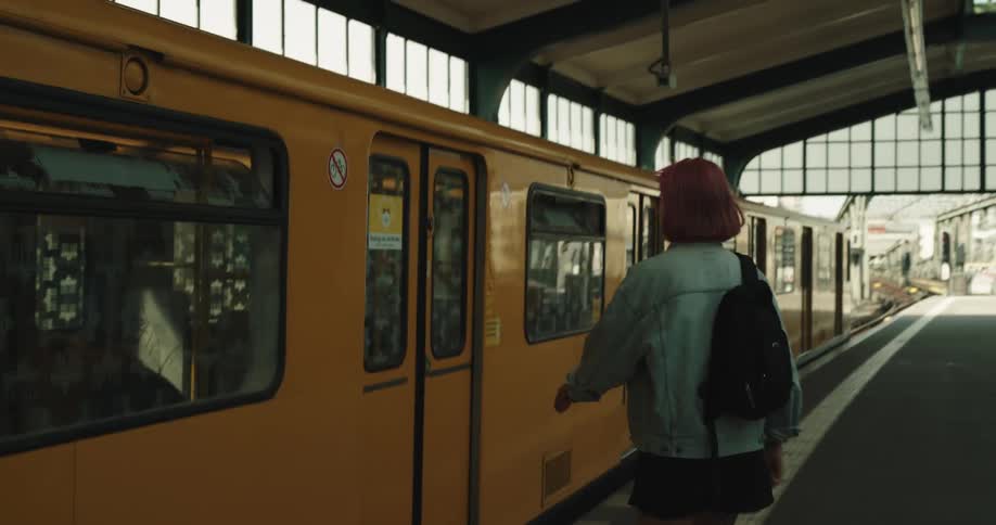 Woman with pink hair denim jacket and black shorts gets on yellow train