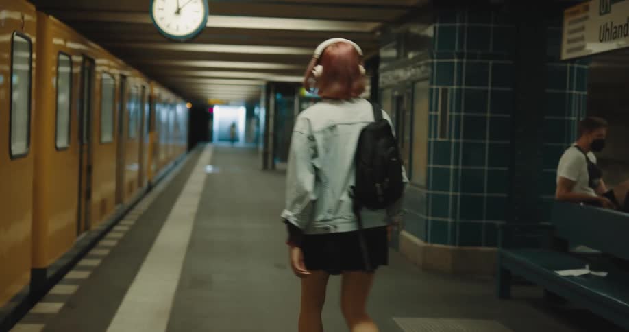 A woman with a backpack and headphones leaving a train and walking on a train station
