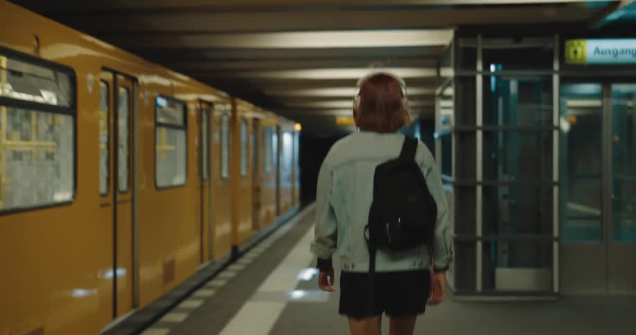 A woman wearing headphones walks down a train station platform