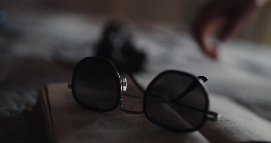 A person picks up their sunglasses and book