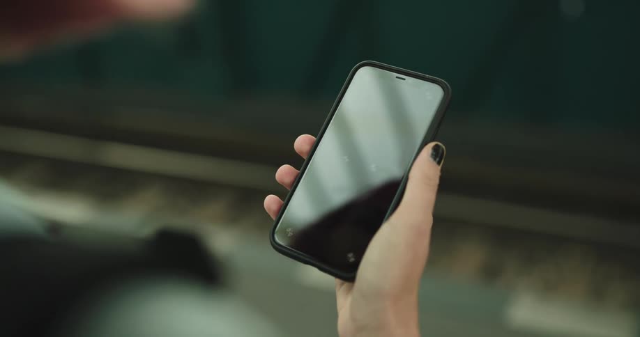 A woman scrolls through her phone while waiting at a train depot