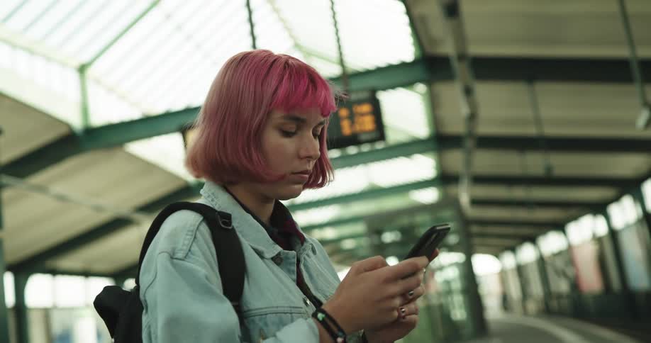 Woman with dyed hot pink hair stands using mobile phone while waiting in terminal for train