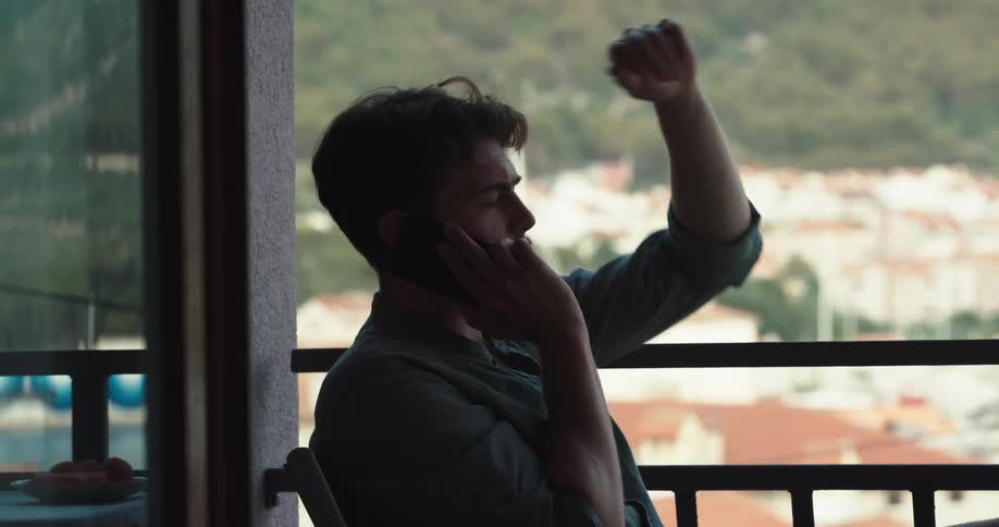 A man is sitting down and he makes a call on his cell phone
