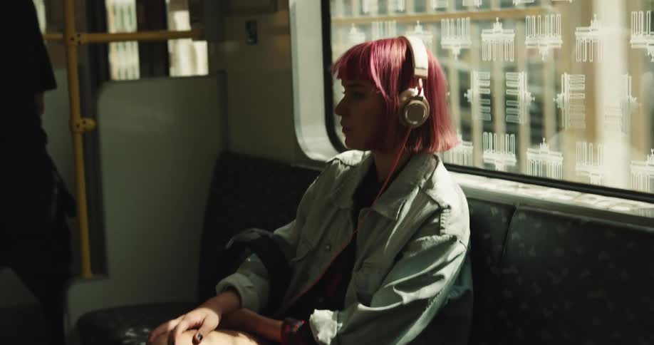 A young woman wearing headphones stands up while riding the subway