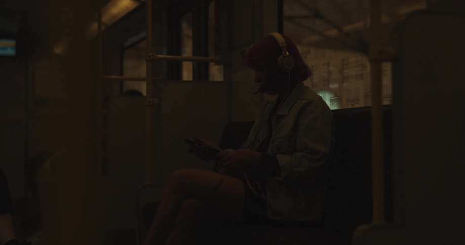 A young woman sitting on the subway puts on headphones and listens to music