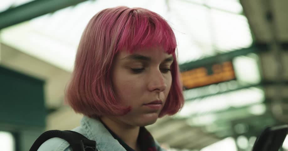 A woman with a backpack on a train station looking at a smart phone with signs in the background