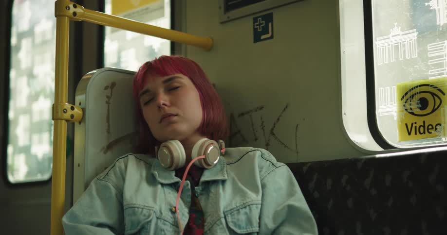 A woman with headphones and a jacket sitting on a train