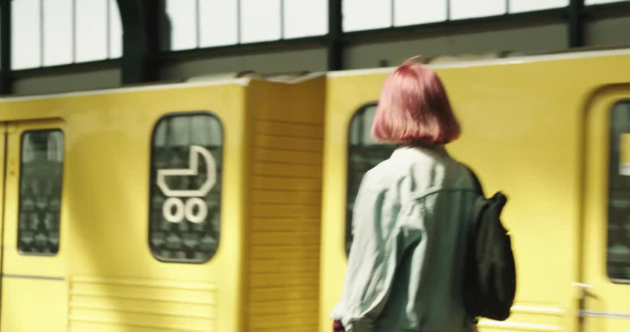 Woman with pink hair denim jacket and black shorts gets on yellow train at the station
