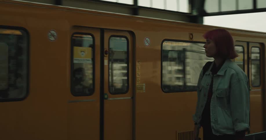 Woman waiting for train stands from bench and boards yellow train car