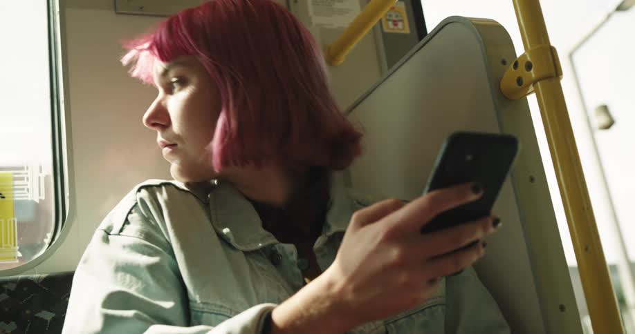 Young woman with short pink hair sitting on a train looking at a phone
