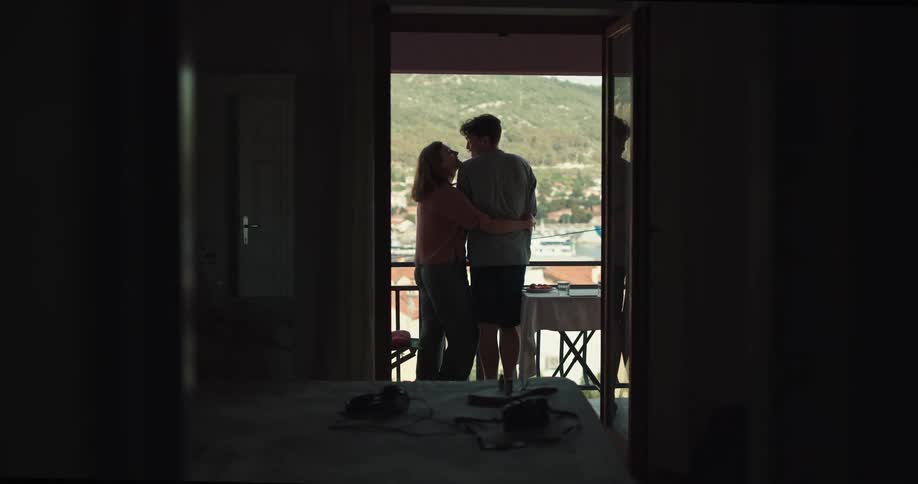 A woman kisses her boyfriend on the balcony of the their hotel room along the coast