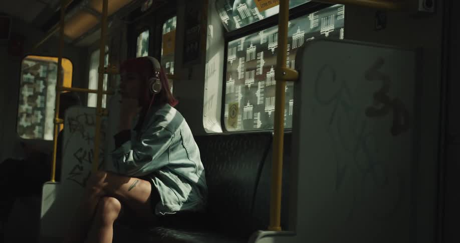 A restless woman is sitting and riding the subway while wearing headphones