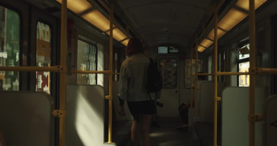 A girl with wine colored hair and wearing a backpack gets on a train and sits down