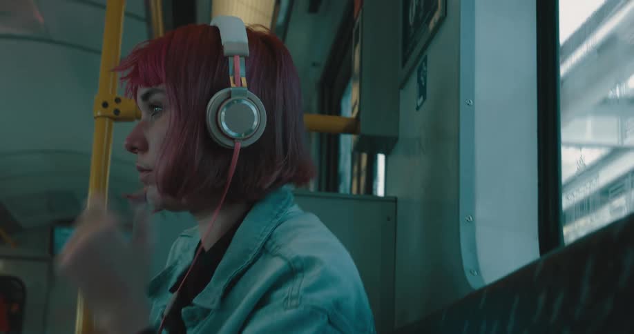 A young woman riding the subway puts headphones on and listens to music