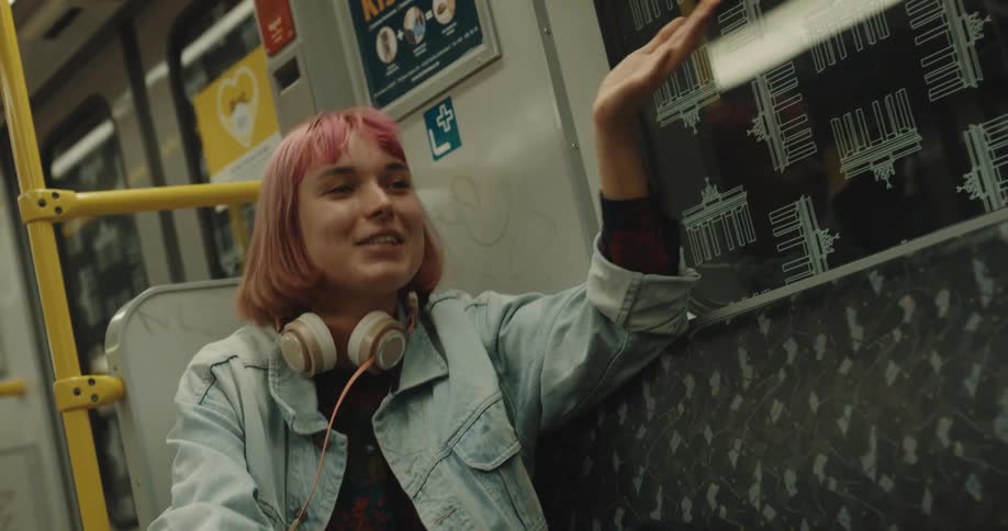 Young woman with short pink hair talking while sitting on a train