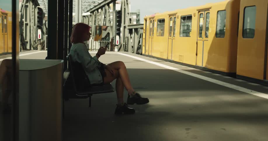A young woman uses her smartphone while sitting on a bench at a train station