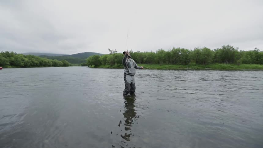 A man stands fly fishing in a river