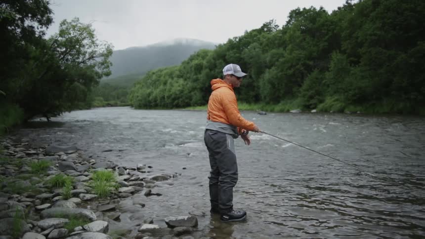 A man in an orange jacket casts his fishing line